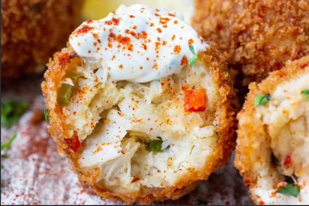 Crispy golden crab balls on a platter with lemon wedges and dipping sauce