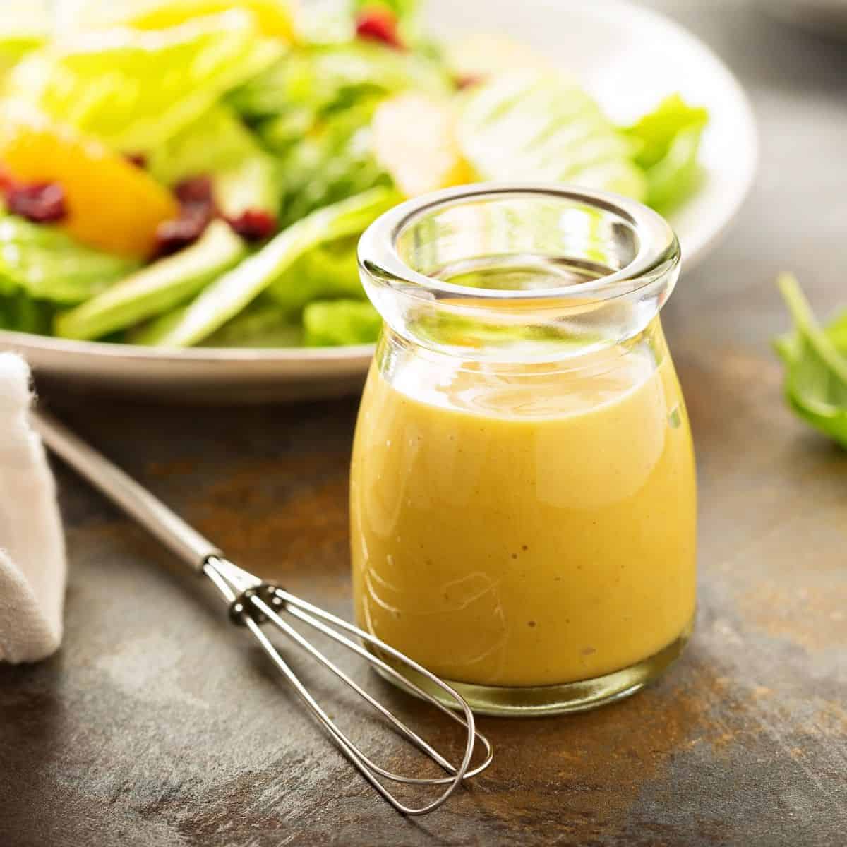 Champagne vinaigrette in a glass jar with fresh herbs and a salad in the background