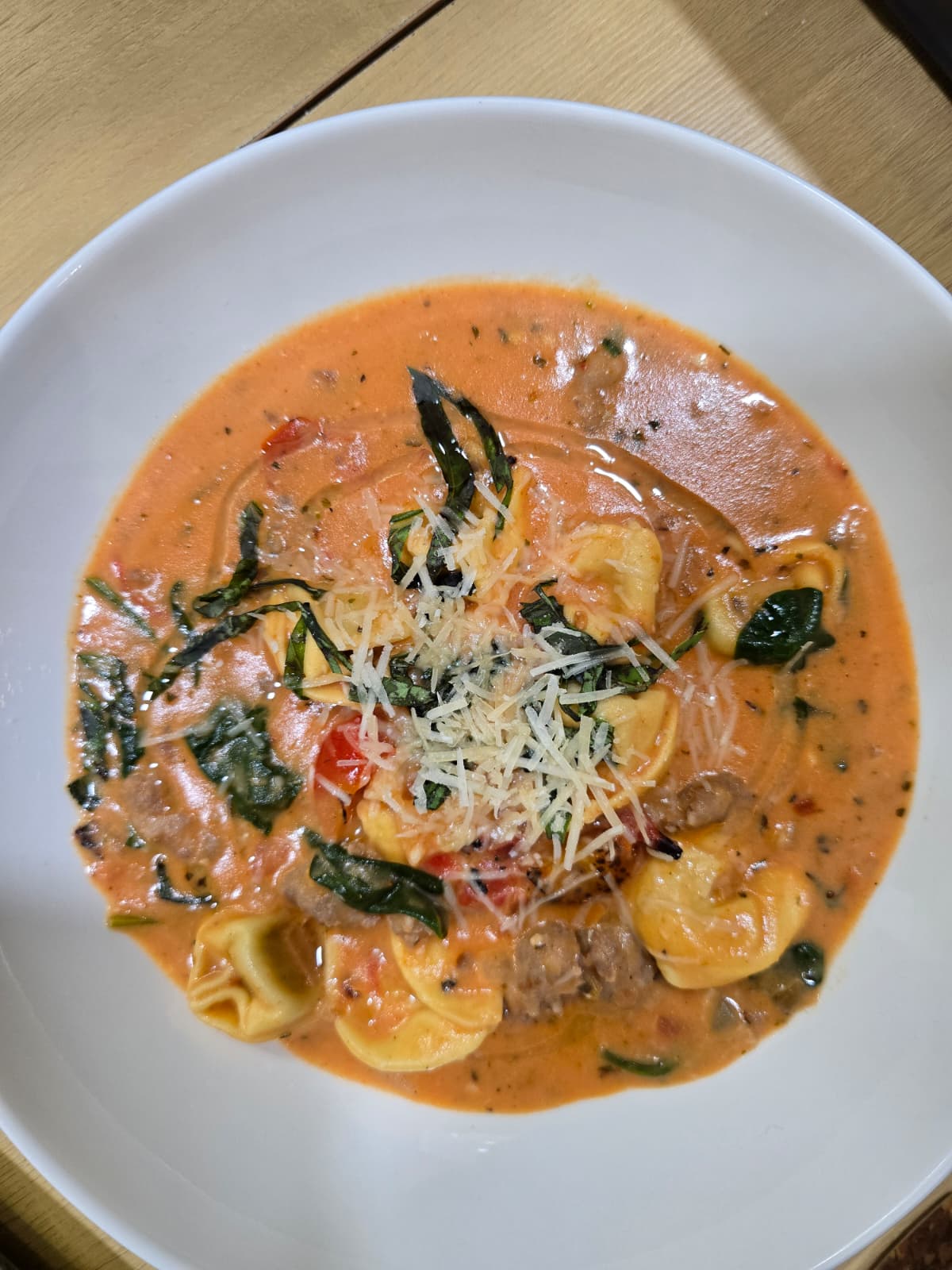 Bowl of creamy sausage tortellini soup topped with Parmesan and fresh basil